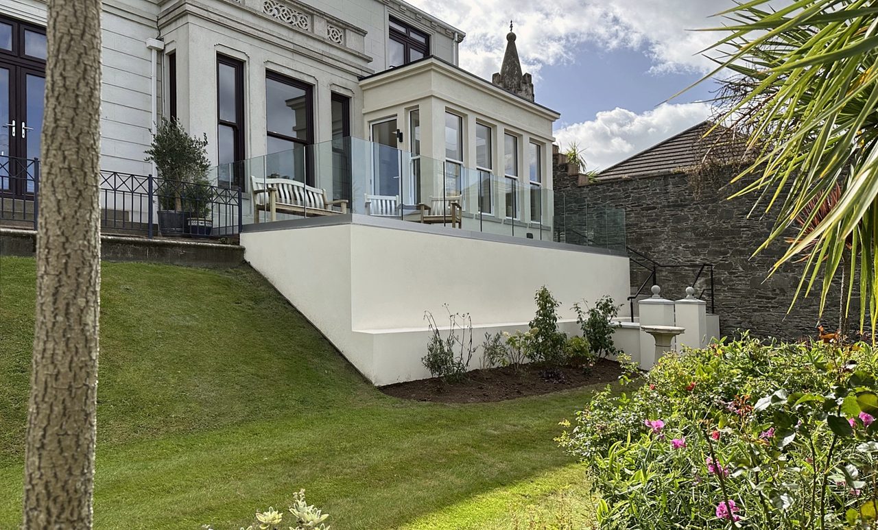 Rendered rear extension and terrace with glass balustrade above a sloping garden
